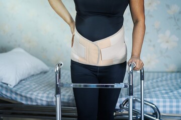 Asian lady patient wearing back pain support belt for orthopedic lumbar with walker. - obrazy, fototapety, plakaty
