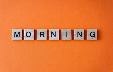 Morning word. The phrase is laid out in wooden letters top view. Orange flat lay background