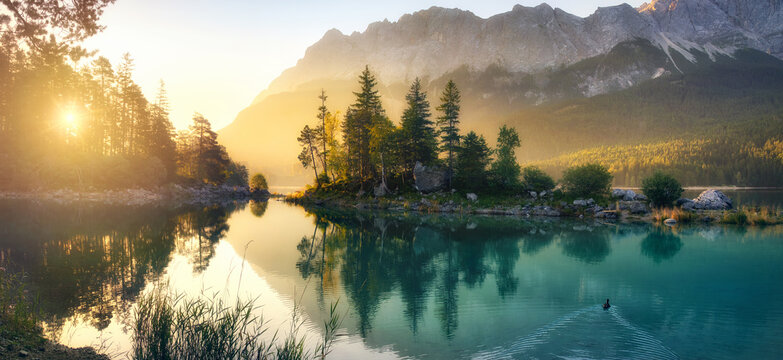 Idyllic lake at sunrise, a picturesque panorama with majestic mountains and the golden sunlight coming in behind the trees