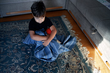 A boy with autism calms down, wrapped in his favorite blanket and sitting on the floor.