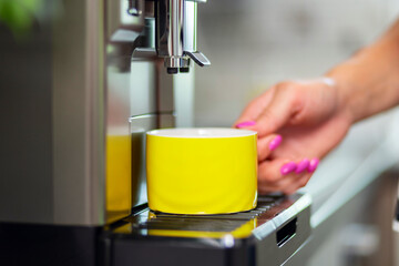 A woman makes fresh flavored coffee with a modern coffee machine in her kitchen