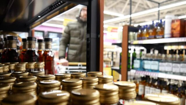 Close-up of many beautiful small bottles of cognac rum or brandy in a liquor store and a male buyer with a shopping trolley walks along a shopping aisle