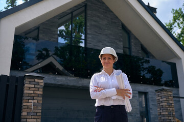 Happy construction supervisor in hard hat standing near new cottage