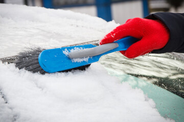 Hand of woman using brush and remove snow from car and windscreen