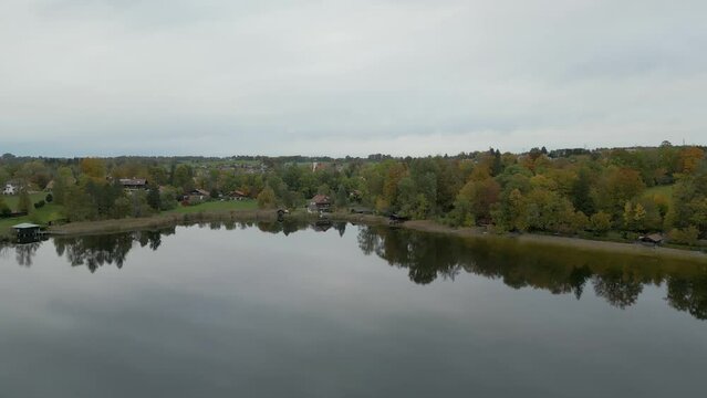 Panning aerial footage of the town of Murnau and the peaceful and placid waters of Staffelsee, reflecting trees and scenery against the amazing backdrop of the German Alps