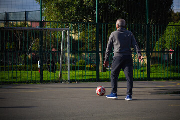 Happy retired senior man kicking a ball playing soccer in a park outside in the afternoon