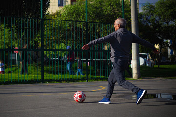 Happy retired senior man kicking a ball playing soccer in a park outside in the afternoon