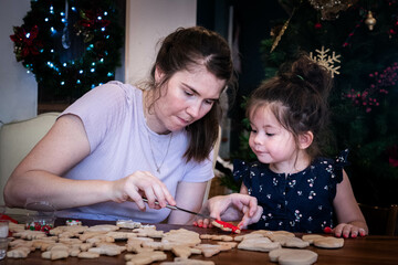 Mother and young daughter sit together and decorate Christmas cookies with icing