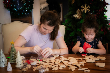 Mother and young daughter sit together and decorate Christmas cookies with icing