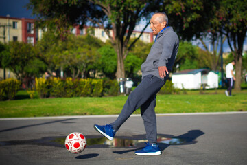 Happy retired senior man kicking a ball playing soccer in a park outside in the afternoon
