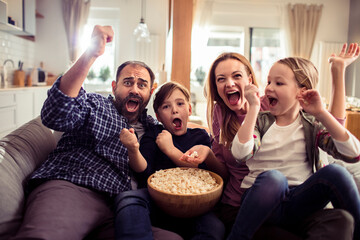 Excited young family watching movie at home on couch