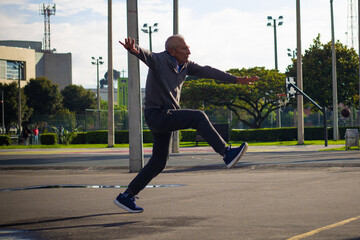 Happy retired senior man kicking a ball playing soccer in a park outside in the afternoon