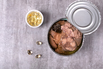 Canned cod liver in metal tin and vitamin D pills on the gray table. Concept of healthy fats and...