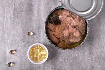 Canned cod liver in metal tin and vitamin D pills on the gray table. Concept of healthy fats and products of nutritional value 