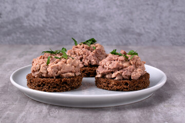 Canape with cod liver on brown bread served on the white plate on gray. Exquisite appetizer