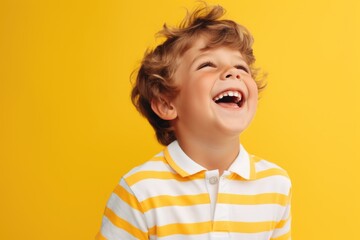 A joyful young boy wearing a yellow and white striped shirt laughs with delight. Perfect for capturing moments of happiness and innocence.