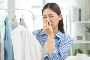 housewife smelling bad odor from damp clothes during laundry.