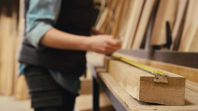 Close up of female carpenter working in woodwork workshop using retractable metal ruler to measure and mark up piece of wood - shot in real time