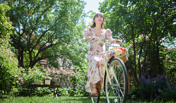 Young and beautiful women ride bicycles in the courtyard full of flowers