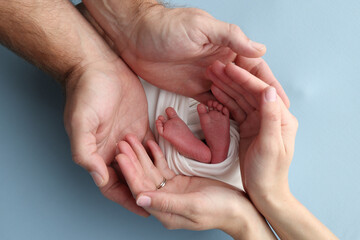 The palms of the parents, father and mother hold the legs, feet of a newborn baby in a white...