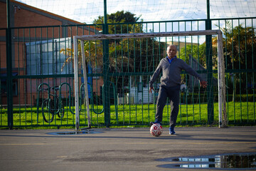 Happy retired senior man kicking a ball playing soccer in a park outside in the afternoon