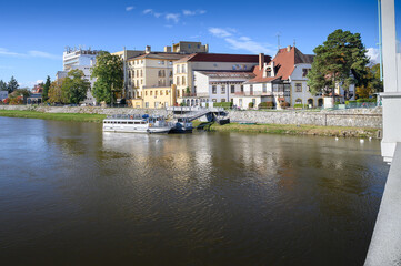 Fototapeta na wymiar View of Vah River with small ship and buildings on riverbank (Piestany, Slovakia)