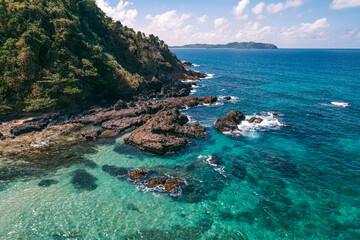 Fototapeta premium Aerial view of waves break on dark rocks near beach. Ocean waves crashing against rocky shore Palawan, Philippines