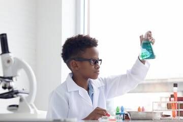 Concentrate African boy in lab coat holds chemical flask for doing science experiment, young...