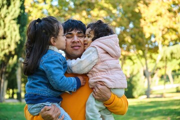 Portrait of happy Ecuadorian kids kissing and hugging his father in a park. Fathers day.