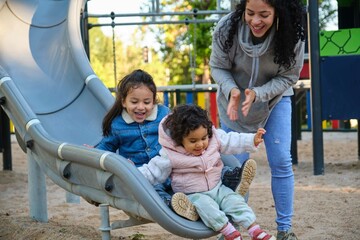 Happy Dominican mother playing with her children at the slide in a park. Latin family.