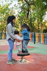 Happy Dominican mother playing with her children at the synchro spinner in a park. Latin family.