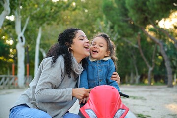Dominican mother and son hugging and laughing on a balance bike in a park. Latin family.