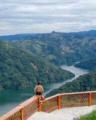 mujer sentada en un mirador viendo de fondo un rio entre montañas verdes en Colombia