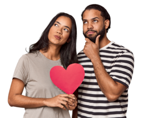 Latina couple with Valentine's sign looking sideways with doubtful and skeptical expression.