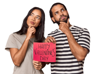 Latina couple with Valentine's sign looking sideways with doubtful and skeptical expression.