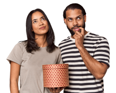 Latina couple with Valentine's heart box relaxed thinking about something looking at a copy space.