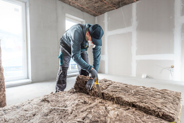 Ceiling insulation. Cutting a thermal insulation from glass wool using a knife for stone wool. iling thermal insulation. - obrazy, fototapety, plakaty
