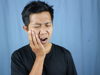 Pain expression of young asian man holding cheek because of toothache. toothache concept