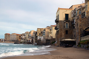 Astonishing coastline view of ancient city Cefalu. Colorful buildings at the sandy beach. Waves of tranquil water splashing against the walls. The Tyrrhenian Sea, Cefalu, Sicily, Italy