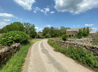 Fototapeta na wymiar View on, Sour Lane, with dry stone walls, wild plants, farm buildings, and old trees, on a sunny day in, Stirton, UK