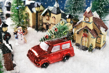 A red car with Christmas tree on the roof in the middle of the street in the small town on snowy...