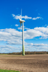 Wind turbine on a field with blue sky and white clouds in portrait format