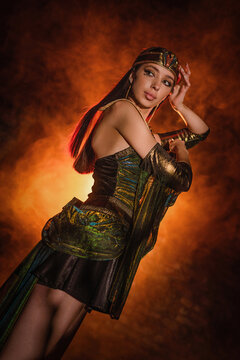 Princess of ancient Egypt girl concept. Young woman posing in the dark on orange smoke background.