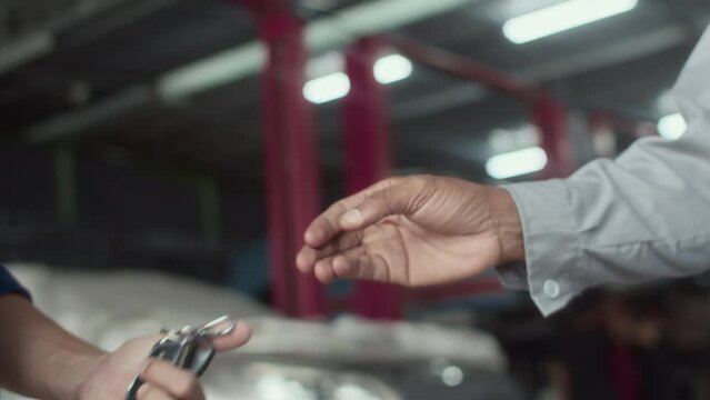 Close up of male repairman giving car keys to owner and shaking hands at service center