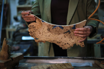 Hands hold a slab of burl wood with intricate grain, highlighting the natural artistry that...