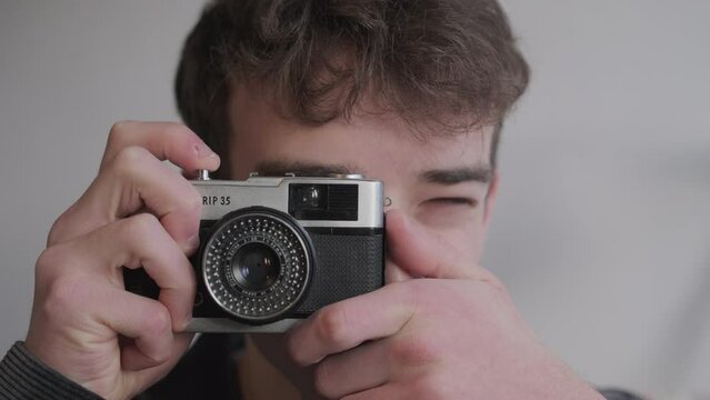 Close up of young man using vintage film camera and then smiling whilst looking at camera