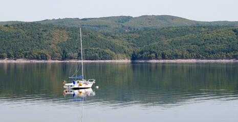 Fototapeta na wymiar Yacht on a mountain lake, high shore reflected in the water