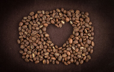 Roasted coffee beans lie in the shape of a heart on a brown background.