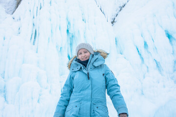Fototapeta na wymiar Happy smiling female wonderer dressed in warm winter clothes posing against of a big ice on the rocks mountain 