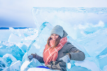 Happy smiling woman traveler
sitting among large pieces of cracked ice floes on a frozen Baikal...
